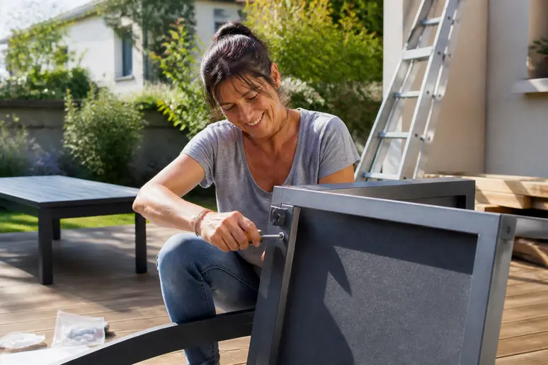 Une Lyonnaise assemble avec plaisir un salon de jardin moderne dans son espace extérieur ensoleillé, appréciant la qualité.