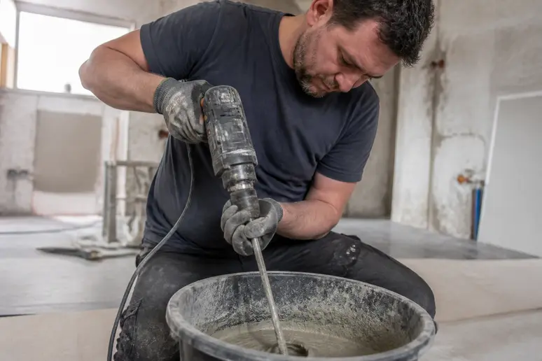 Artisan français mélangeant du ciment et de l'eau dans un seau à l'aide d'un malaxeur pour obtenir une barbotine homogène.