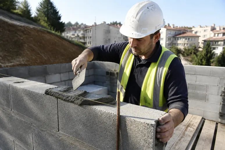 Un maçon français pose des blocs de parpaing pour ériger un mur, illustrant le choix économique pour la construction structurelle.