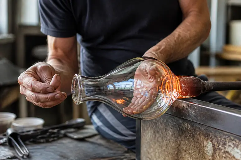 Mains d'artisan travaillant le verre soufflé dans un atelier français, illustrant le savoir-faire traditionnel et la beauté des matériaux.