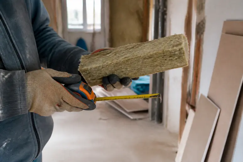 Gros plan sur des mains gantées tenant un mètre et de la laine de verre ou roche