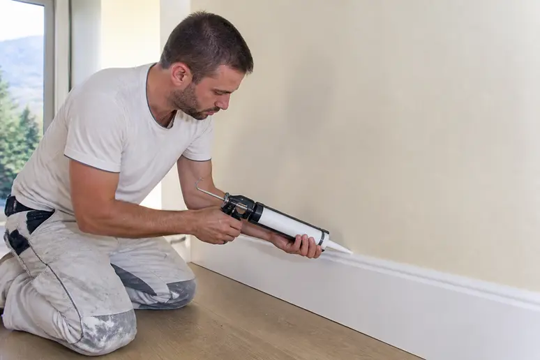 Poseur appliquant un joint acrylique pour parfaire la finition après avoir posé des plinthes.
