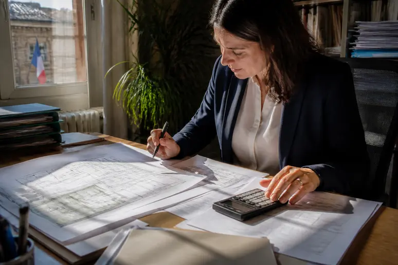 Agent vérifiant des plans et calculant la taxe d'aménagement pour le prix dalle beton.