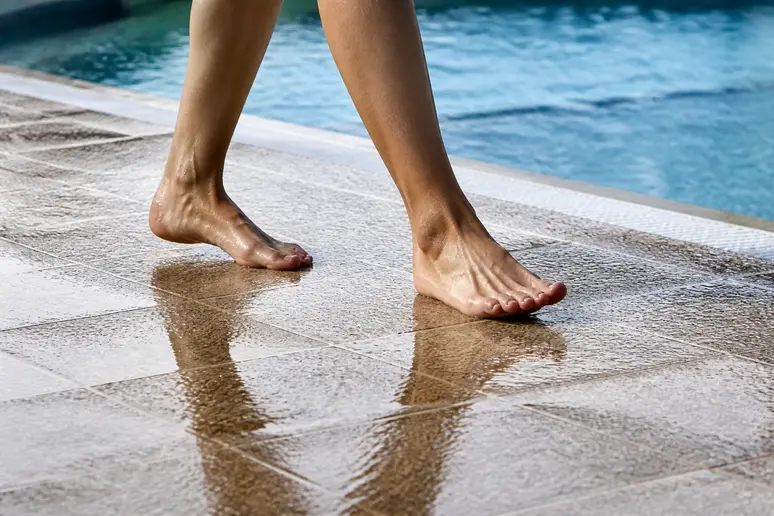 Pieds nus marchant sur des dalles de carrelage antidérapant R11 au bord d'un bassin