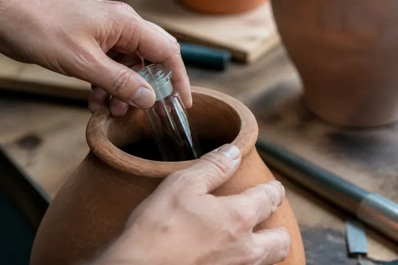 Mains insérant une fiole en verre étanche dans un vase en terre cuite brute